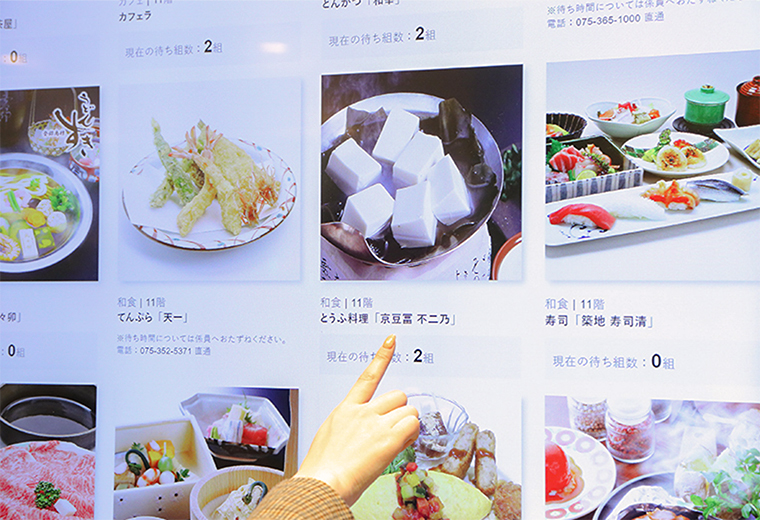 写真:サイネージで各店舗の待ち組数を確認している様子